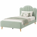 Cama individual tapizada en tela verde con patas de madera